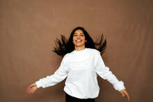 Positive ethnic female in white sweatshirt and with flying hair having fun in studio with closed eyes