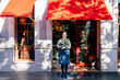 © Javier Ballester/ADDICTIVE STOCK - Woman holding flower bouquet standing outside shop with christmas decorative baubles and garlands in daylight looking at camera