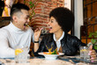 © Jose Carlos Cerdeno/ADDICTIVE STOCK - Laughing African American young woman feeding cheerful Asian boyfriend with salad while having fun during lunch in cafe