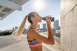 © Jordi Bataller/ADDICTIVE STOCK - Side view of thirsty female athlete drinking fresh water from bottle while standing on street and having break during training
