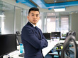 © Jose Carlos Cerdeno/ADDICTIVE STOCK - Side view of serious young Asian male manager in formal suit looking at camera while standing near table with computers in contemporary coworking office