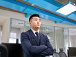 © Jose Carlos Cerdeno/ADDICTIVE STOCK - Serious young Asian male manager in formal suit looking away while standing near table with computers in contemporary coworking office