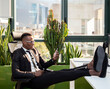 © Jose Carlos Cerdeno/ADDICTIVE STOCK - Full body side view of positive young ethnic black male employee in casual outfit sitting on chair with legs on table and messaging on smartphone while resting during break in modern workspace