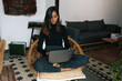© Joy Zamora/ADDICTIVE STOCK - Serious Indian female freelancer sitting with crossed legs in wicker chair and typing on netbook while working online from home