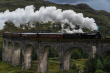 Old Fashioned Steam Train Riding Along Glenfinnan Viaduct Located In Mountains On Cloudy Day In Scotland