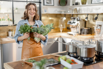 Portrait of pretty smiling woman with fresh vegetables in beautiful design interior of kitchen. Housewife cooking healthy dinner. High quality photo