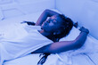 © Julio Rodriguez/ADDICTIVE STOCK - Young black woman sleeping on bed in contemporary capsule hotel with futuristic interior design and blue illumination