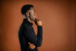 © Luis Manuel Munoz/ADDICTIVE STOCK - Side view of pensive African American male rubbing chin and leaning on hand while standing on brown background in studio and looking away