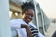 © Luis Gomez/ADDICTIVE STOCK - Cheerful young black female student with Afro hairstyle wearing casual clothes looking at camera while sitting near fence on urban embankment and enjoying summer day