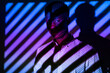 © Luis Manuel Munoz/ADDICTIVE STOCK - Unemotional African American male standing in neon light in shape of stripes in dark studio and looking at camera