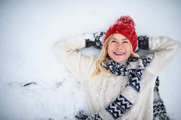 Top view portrait of senior woman with hat outdoors lying on snow, looking at camera.