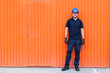 © Manuel Ruiz/ADDICTIVE STOCK - Positive confident adult male workman in blue protective hardhat and eyeglasses while standing against bright orange wall of workshop
