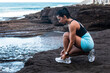 © Pablo Garcia/ADDICTIVE STOCK - Side view of fit ethnic female athlete tying shoelaces on sneakers while sitting on seashore and preparing for workout