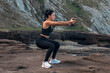 © Pablo Garcia/ADDICTIVE STOCK - Side view of glad female athlete in sportswear doing squat exercise with rock while training in nature in summer