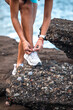 © Pablo Garcia/ADDICTIVE STOCK - Ethnic female athlete tying shoelaces on sneakers while sitting on seashore and preparing for workout