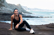 © Pablo Garcia/ADDICTIVE STOCK - Delighted fit female in activewear sitting on beach on background of amazing seascape and looking at camera after workout