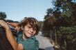 © Mireia Cordomi/ADDICTIVE STOCK - Side view of preteen boy with curly hair sitting in open window of automobile and looking away while enjoying summer adventure in mountainous land