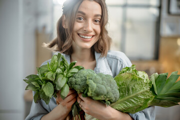 Portrait of pretty smiling woman with fresh broccoli, roman salad, basil on the kitchen. Healthy green vegetable concept. Close up. High quality photo