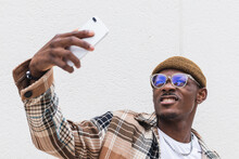 Trendy African American Male In Casual Clothes And Glasses Frowning And Taking Selfie Against Gray Wall On City Street