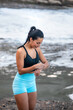 © Pablo Garcia/ADDICTIVE STOCK - High angle of content sportswoman standing on seashore and checking pulse on modern smart watch during active workout in summer
