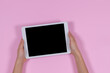 Hands holding digital tablet computer on pastel pink background