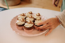 Crop Anonymous Female Confectioner Putting Delectable Chocolate Cupcakes With Whipped Cream On Plate Placed On Table