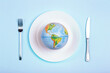 Globe on a plate for food on a blue background. Power, economy, politics, globalism, hunger, poverty and world food concept