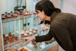 © Raquel Arocena/ADDICTIVE STOCK - Side view of happy young female customer pointing at cupcake on display of confectionery shop while choosing sweets for purchase