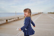 © Santi Miquel/ADDICTIVE STOCK - Side view of adorable cheerful little girl in blue dress with toy on hand having fun on paved walkway in summer day