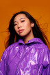 © Victor Torres/ADDICTIVE STOCK - Portrait of Asian young woman with serious expression. She wears a purple jacket and a gray cap and is looking at the camera against a yellow background
