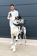 © Sergio Victor Vega/ADDICTIVE STOCK - Smiling male standing on street with Harlequin Great Dane dog and messaging on social media while entertaining at weekend in city