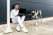 © Sergio Victor Vega/ADDICTIVE STOCK - Male freelancer sitting on street with Great Dane dog and working on remote project via laptop