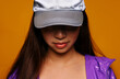 © Victor Torres/ADDICTIVE STOCK - Portrait of Asian young woman. She wears a purple jacket and a grey cap and is looking away smiling against a yellow background