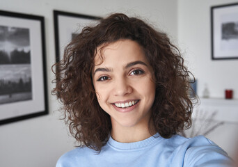 smiling cute cheerful young pretty hispanic latin woman looking at camera standing alone at home. ha