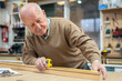 © The Trio Studio/ADDICTIVE STOCK - Elderly male woodworker measuring material with tape placed on machine in joiner