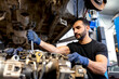 © Sergio Victor Vega/ADDICTIVE STOCK - Busy bearded male mechanic with metal wrench repairing dirty car engine in modern service