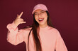 © Victor Torres/ADDICTIVE STOCK - Portrait of happy young asian woman in the studio wearing pink clothes over garnet background. She is winking and making the rock sign