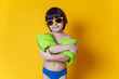 © saulich84 - boy child in inflatable green swim armbands and sunglasses stands on a yellow background in the studio