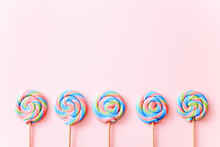 Colorful Lollipops Swirls On Sticks In Row. Striped Spiral Multicolored Candy On Pink Background, Top View