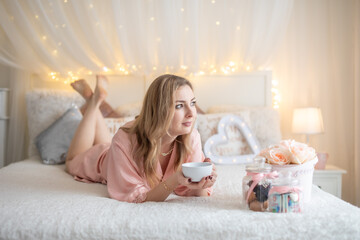 Sexy young girl laying in white bed with flowers and tea - gift for February 14 or March 8