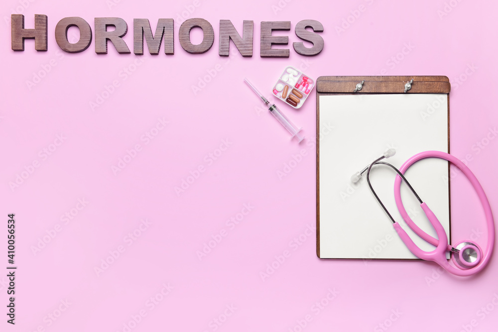Word HORMONES, stethoscope, syringe and pills on color background