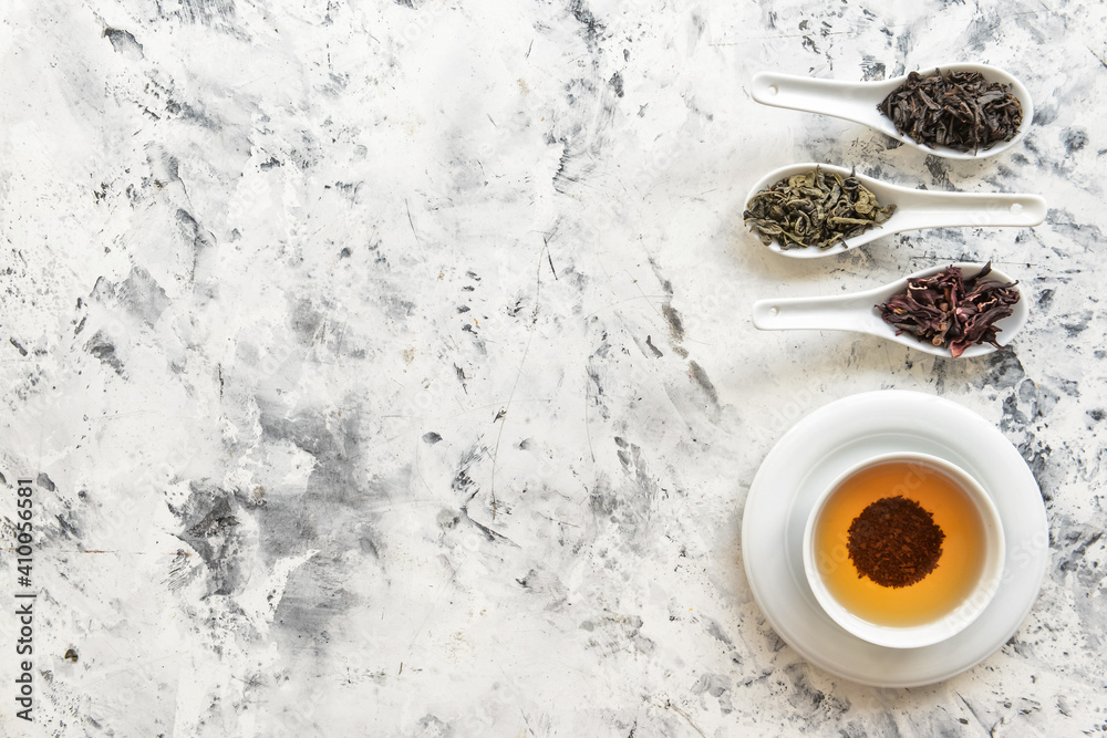 Cup of tea and spoons with different dry leaves on light background