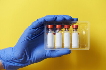 a hand in a medical glove holds several test tubes. Coronavirus vaccination, laboratory tests