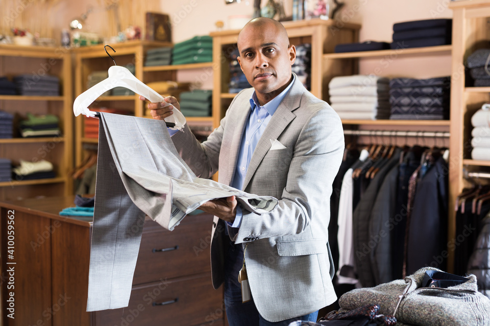 Portrait of young adult man choosing suit pants to new jacket in clothing store - obrazy, fototapety, plakaty 