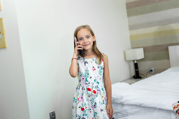 Little girl is talking on the phone in a hotel room