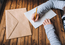 Children's Hands Write A Letter. A Brown Envelope, A White Sheet Of Paper And A Pencil. Distance Education Concept.