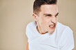 © SHOTPRIME STUDIO - Man with displeased facial expression emotions white t-shirt gestures with hands beige background