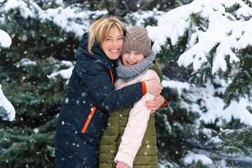 mother and daughter family portrait in a winter forest, one parent and one children, beautiful nature with bright snowy fir trees