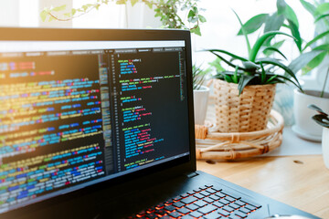 St Petersburg, Russia - 30 Jan 2021: Html code on the laptop screen standing on a wooden table with home green plants, cozy working office. Selective focus