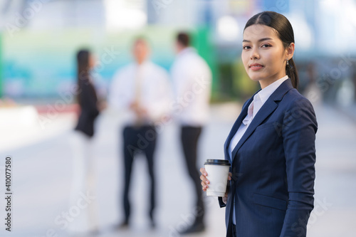 Portrait of smiling business woman holding a coffee cup while standing in front of modern office © Naypong Studio